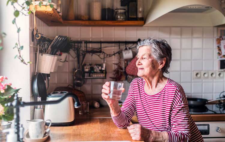 an elderly woman standing in the kitchen holding