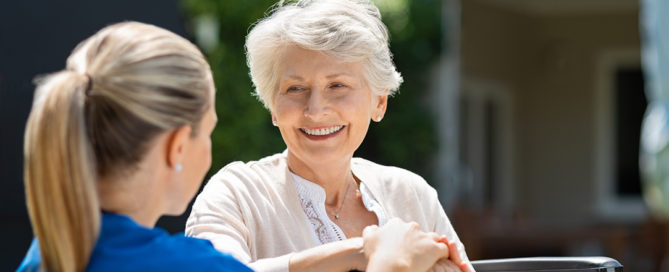 senior woman on wheelchair smiling at her caregiver