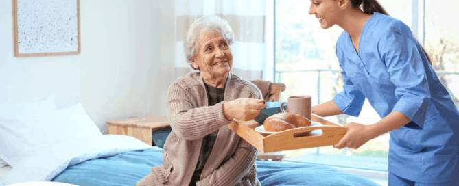 A professional caregiver smiles and provides food to an older adult in her care, representing the compassionate care needed for those with dementia.