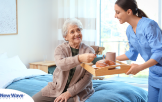 A professional caregiver smiles and provides food to an older adult in her care, representing the compassionate care needed for those with dementia.