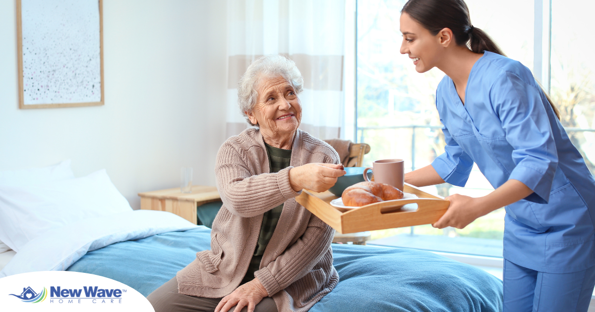 A professional caregiver smiles and provides food to an older adult in her care, representing the compassionate care needed for those with dementia.