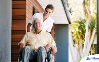 A caregiver brings an elderly man in a wheelchair out of a building, demonstrating a hospital discharge.