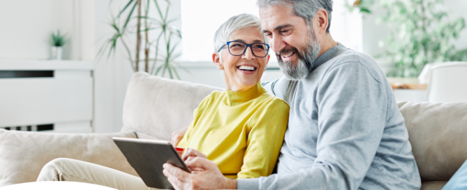 A senior couple smiles while looking at a laptop, showing how online resources can help family caregivers.