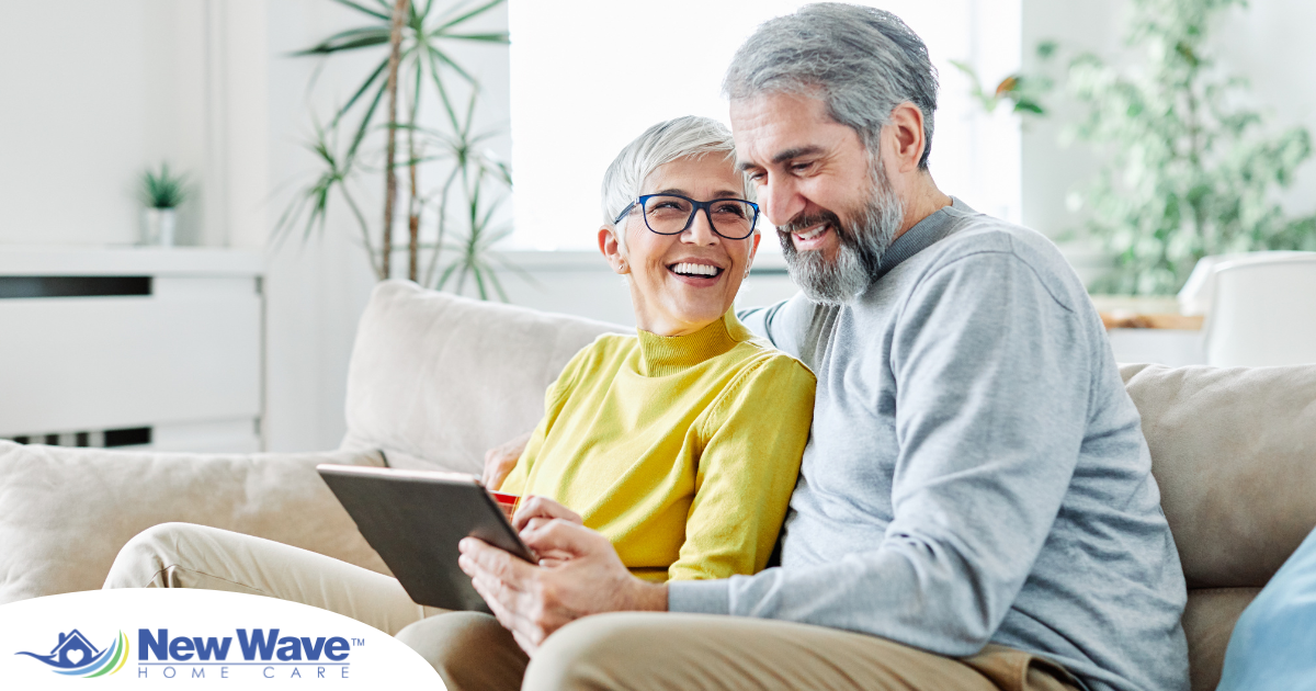 A senior couple smiles while looking at a laptop, showing how online resources can help family caregivers.