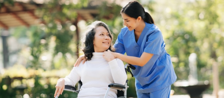 A caregiver kindly helps an older client in a wheelchair, representing how New Wave's respite care services can help those in Los Angeles.