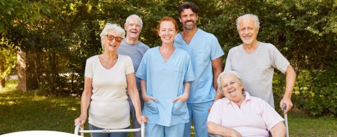 2 caregivers and seniors smile while in a group representing how caregivers can facilitate socialization.