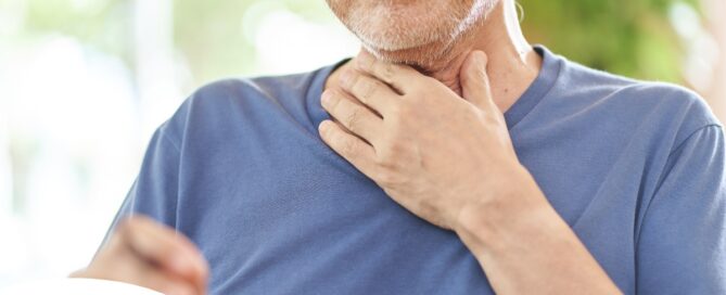 An older adult holds his throat representing dysphagia which can affect senior health.