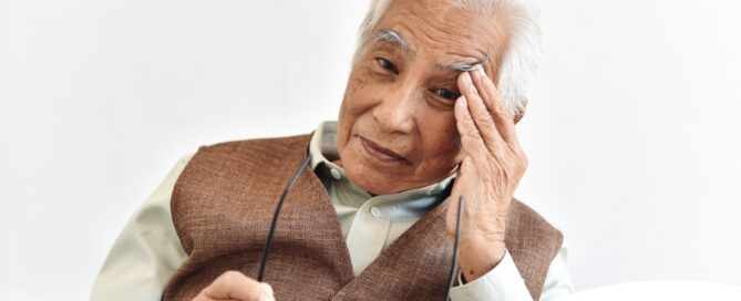 An older adult holds his head and his glasses representing vision problems like macular degeneration.