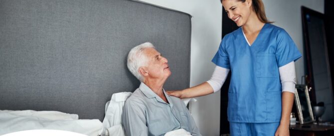 A caregiver smiles at an older client in bed, representing the compassion involved in being a live-in caregiver.