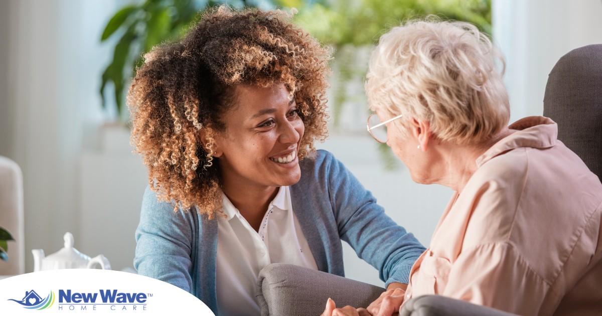 A caregiver smiles at an older client in a chair, representing the joy that can come from a healthy work-life balance.