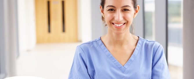 A woman in scrubs smiles, representing the good results that can come when caregivers branch out to become CNAs.