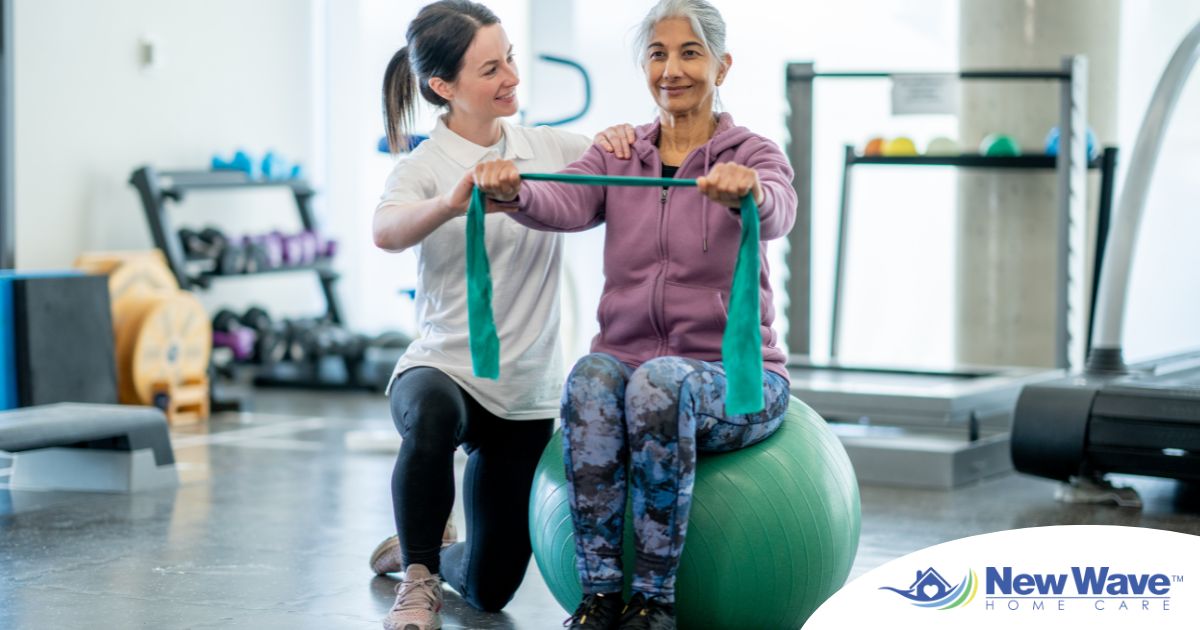 A care provider helps an older woman exercise with a resistance band and an exercise ball, representing how exercise can help with senior fall prevention.